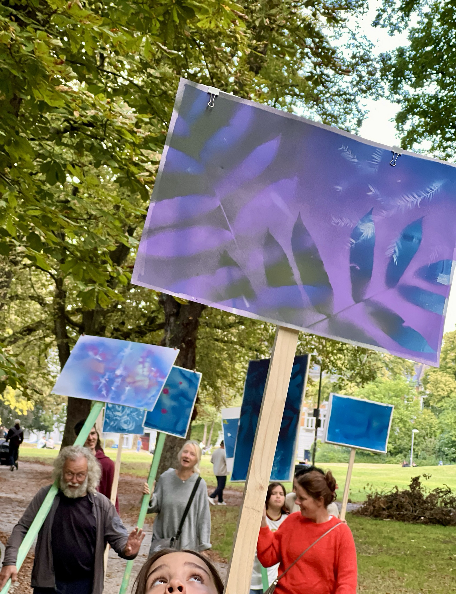 Gruppe von Menschen unterschiedlichen Alters geht in einem Park und trägt bunte Schilder mit abstrakten Mustern