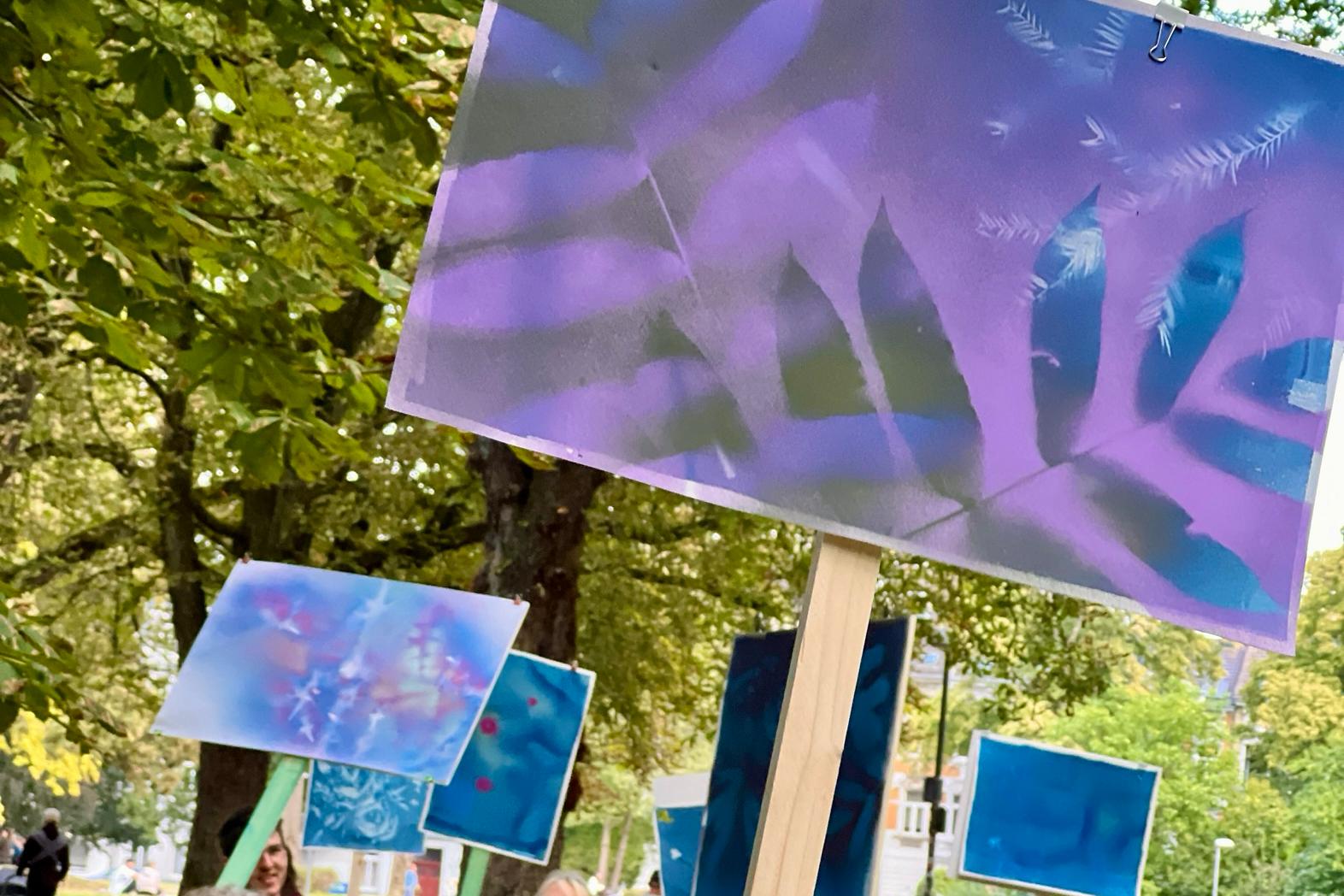 Gruppe von Menschen unterschiedlichen Alters geht in einem Park und trägt bunte Schilder mit abstrakten Mustern